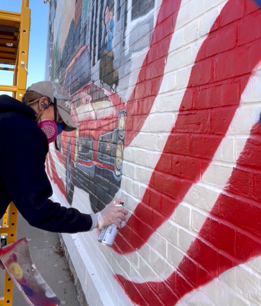 An artist paints a mural on the side of a building.
