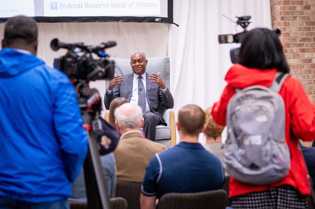 Atlanta Fed President Raphael Bostic sitting in a chair talking to an audience at a speaking engagement.