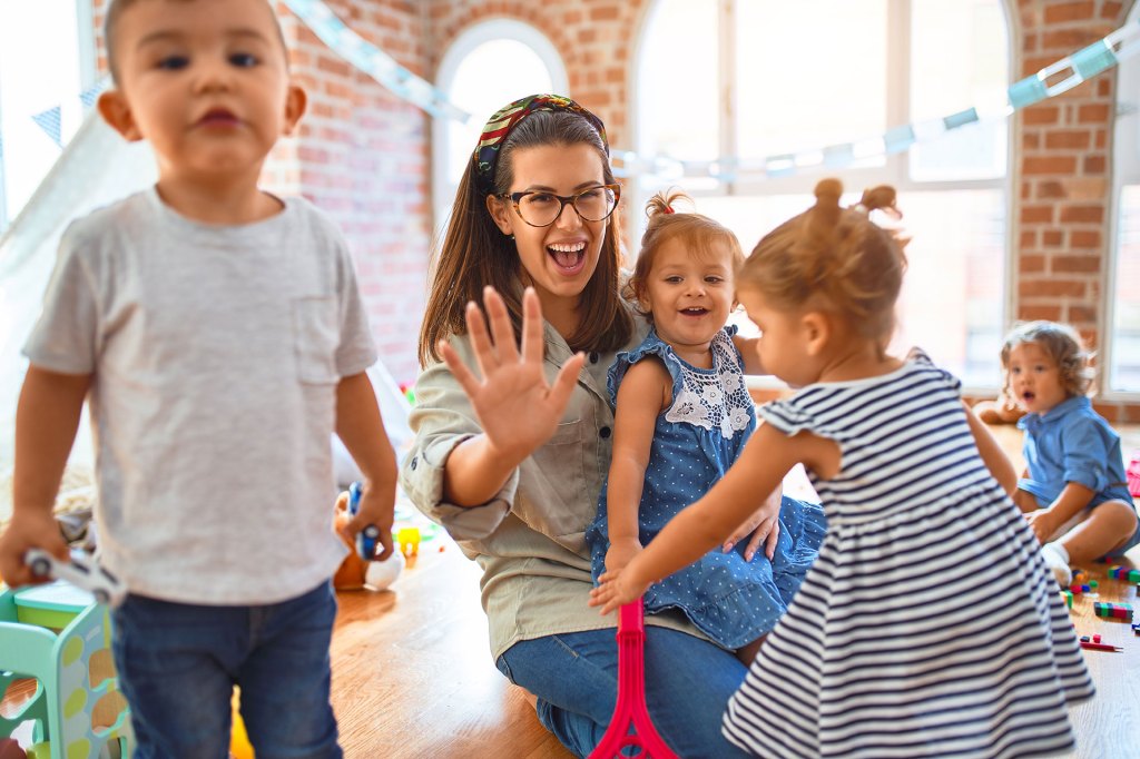 Daycare teacher and group of toddlers playing around lots of toys at her in home daycare facility.